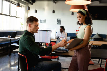Multiracial businessman and businesswoman discussing over file in creative office. Unaltered,...