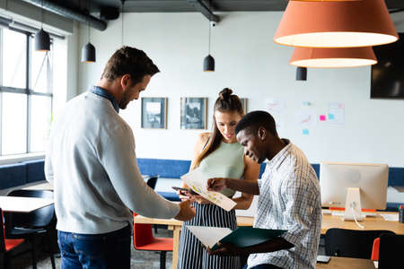 Multiracial colleagues discussing strategy over charts in creative office. Unaltered, creative business, workplace, occupation, diversity, meeting, planning, teamwork.の写真素材