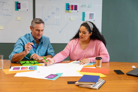 Multiracial businessman and businesswoman discussing strategy over documents in creative office....
