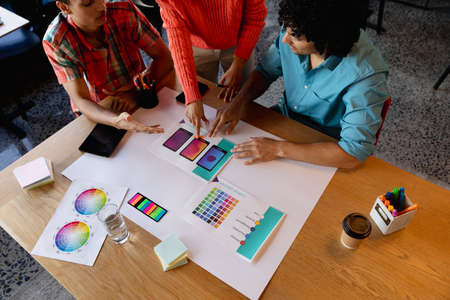 Creative multiracial male and female colleagues discussing over charts in office. Unaltered,...