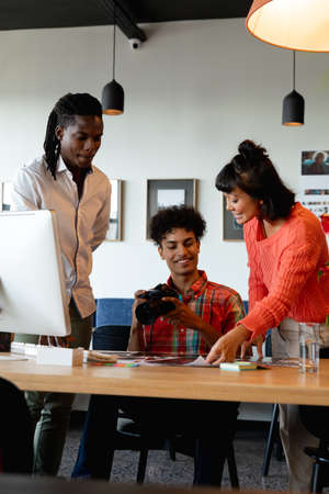 Biracial photographer discussing with multiracial colleagues in meeting at creative office....