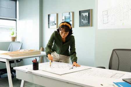 Asian young female architect drawing blueprint at table in creative office. Unaltered, workplace, creative business, design professional, floor plan.の写真素材