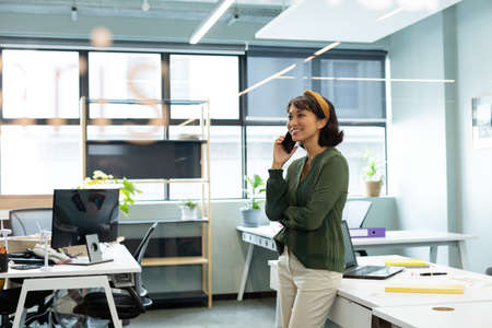Smiling asian female architect talking on mobile phone in creative office. Unaltered, workplace,...