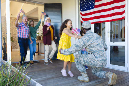 Excited multiracial multigeneration family with flag of america welcoming army soldier in house. Happy, military, welcoming, unaltered, family, love, togetherness, childhood and patriotism concept.