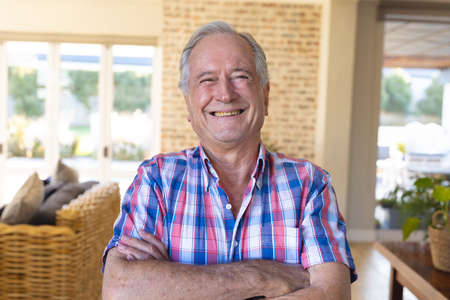 Portrait of smiling caucasian senior man with arms crossed wearing checked pattern shirt in home....