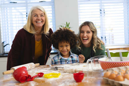 Portrait of cheerful multiracial multigeneration family preparing food on messy table in kitchen....