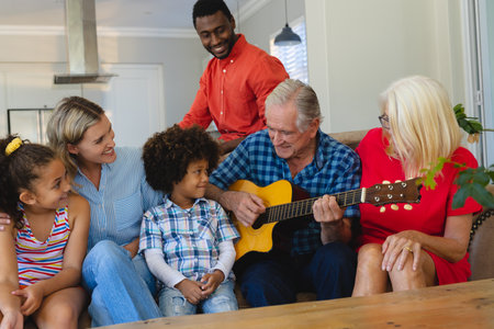 Happy multiracial multigeneration family looking at senior man playing guitar while sitting on sofa....