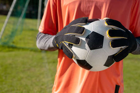 Midsection of african american male goalkeeper wearing gloves holding soccer ball at playground. Defending, unaltered, soccer, competition and sport concept.の写真素材