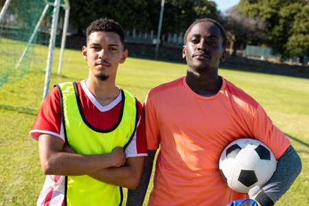 Portrait of serious multiracial players with arms crossed and holding ball standing in playground....