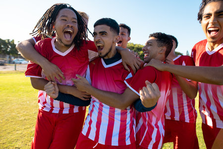 Multiracial male team players screaming while celebrating victory after soccer match at playground. Unaltered, soccer, sport, teamwork, togetherness, competition, winning, happy and achievement.の写真素材