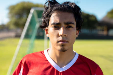 Close-up portrait of confident serious young male soccer player in red jersey at playground. Summer, face, blond hair, unaltered, soccer, competition and sport concept.の写真素材
