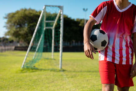 Midsection of caucasian male player wearing red jersey with soccer ball standing on grassy land. Playground, summer, unaltered, soccer, competition, training and sport concept.の写真素材