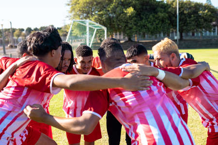 Multiracial male team players in red uniforms huddling and discussing at playground during match. Summer, motivation, meeting, unaltered, soccer, sport, teamwork, togetherness and competition.の写真素材