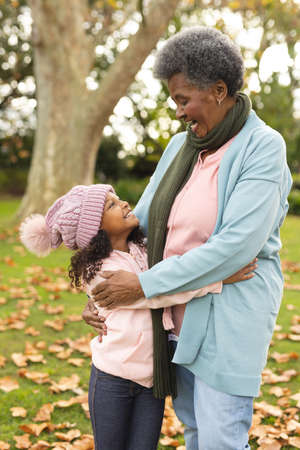 Vertical image of happy african american grandmother and granddaughter embracing in garden. Family and spending quality time together concept.の写真素材