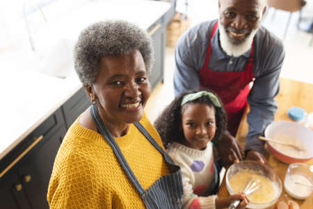 Image of happy african american grandparents and granddaughter baking in kitchen. Family and...