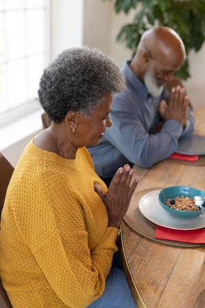 Vertical image of senior african american couple praying before meal. Family and spending quality time together concept.の写真素材