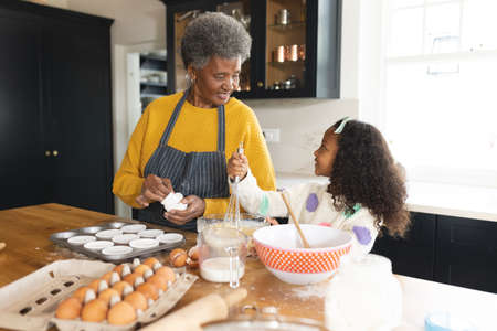 Image of happy african american grandmother and granddaughter baking in kitchen. Family and spending...