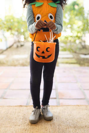 Vertical image of midsection of african american girl in halloween costume with basket. Halloween, american culture and celebration concept.の写真素材