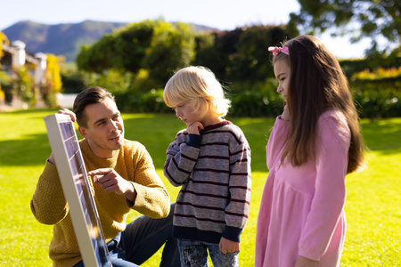 Image of caucasian father showing solar panel to children. Family, green energy, eco awareness and...
