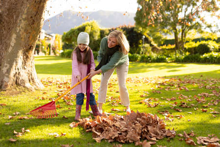 Image of happy caucasian grandmother and granddaughter swiping leaves in garden. Family and spending quality time together concept.の写真素材