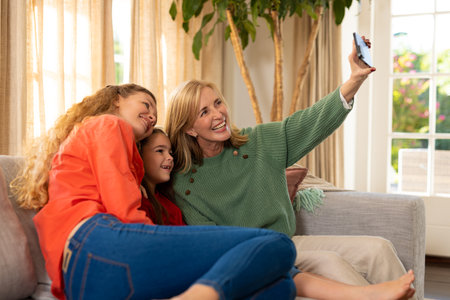 Image of happy three generation caucasian women sitting on sofa and taking selfie. Family and...