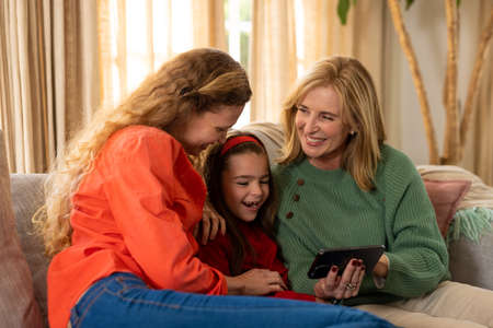 Image of happy three generation caucasian women sitting on sofa and using smartphone. Family and spending quality time together concept.の写真素材