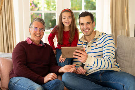 Image of happy caucasian grandfather, father and daughter sitting on sofa with tablet. Family and...