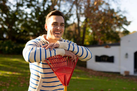 Image of happy caucasian man with rake in garden. Lifestyle, autumn, spending time at home and garden concept.の写真素材