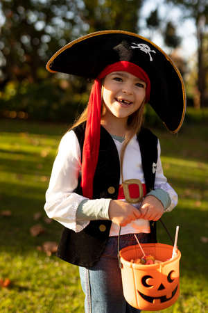 Vertical image of happy caucasian boy in pirate costume in autumn garden. Halooween, american culture and celebration concept.の写真素材