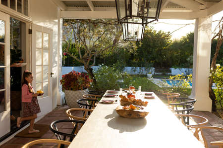 Image of caucasian girl preparing outdoor dinner on patio. Childhood, responsibilities and helping at home concept.の写真素材