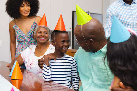Happy multiracial multigeneration family wearing colorful party hats while enjoying birthday at...