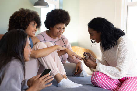 Biracial young woman painting female's fingernails while spending leisure time with friends on...