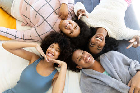 High angle portrait of happy biracial young female friends gesturing and lying while relaxing on bed. Unaltered, friendship, togetherness, lifestyle and home concept.の写真素材