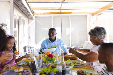 Multiracial multigeneration family eating lunch while sitting at dining table at home. Meal, decoration, drink, food, unaltered, togetherness, love, childhood, lifestyle and retirement concept.の写真素材