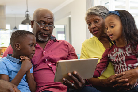 Multiracial grandparents with grandchildren watching video over digital tablet while sitting at...
