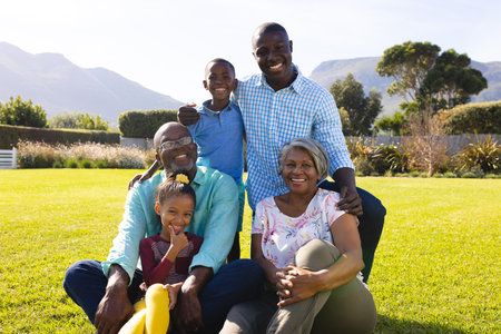 Portrait of happy multiracial multigeneration family enjoying leisure time on grassy field in yard....