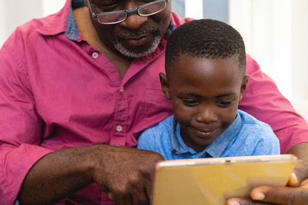 Midsection of multiracial grandfather and grandson using digital tablet while sitting at home....