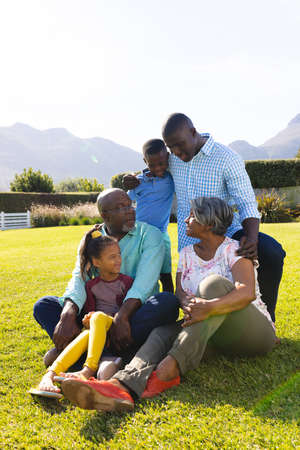 Multiracial multigeneration family talking while enjoying leisure time on field against clear sky....