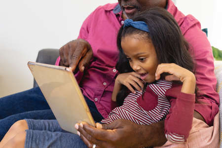 Midsection of multiracial grandfather with granddaughter watching video over digital tablet at home. Wireless technology, unaltered, family, togetherness, childhood and retirement concept.の写真素材
