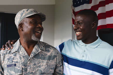 Happy african american military senior man looking at smiling mid adult son against house. Family, togetherness, unaltered, pride, military, armed forces, patriotism, homecoming, camouflage clothing.の写真素材