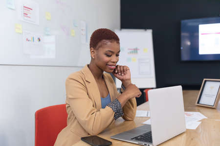 Smiling african american young businesswoman sitting with laptop in board room. Unaltered, creative business, workplace, office, communication, wireless technology.の写真素材