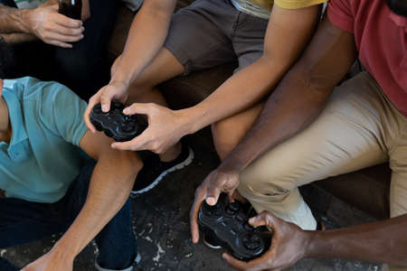 Midsection of multiracial male friends with controller playing video game while sitting at home....