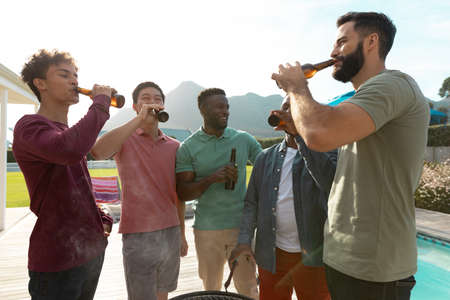 Carefree male multiracial friends having beer while chatting in barbecue party at yard, copy space....