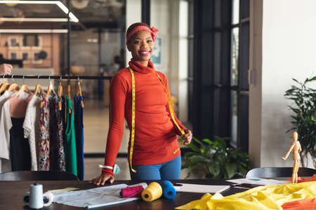 Portrait of smiling african american fashion designer at desk in studio office. Unaltered, creative business, wireless technology, fashion, workplace, positive emotion.の写真素材