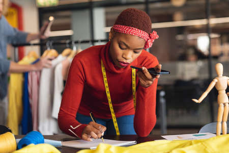 African american young female fashion designer taking order through mobile phone in studio office. Unaltered, creative business, wireless technology, fashion, workplace, ordering.の写真素材