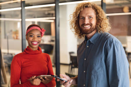 Portrait of smiling multiracial male and female colleagues with smart phones in office. Unaltered, creative business, positive emotion, wireless technology, workplace.の写真素材