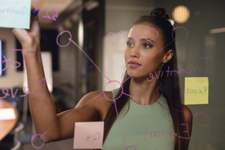 Caucasian young businesswoman writing business strategy on glass in creative office. Unaltered,...