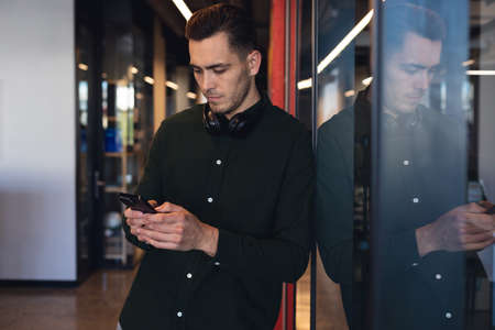 Caucasian young businessman using internet in smart phone at creative office. Unaltered, creative...