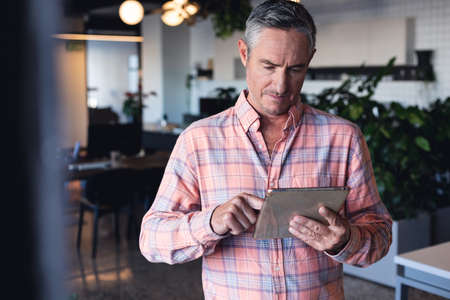 Caucasian mature businessman using digital tablet in creative office. Unaltered, creative business, wireless technology, internet, communication.の写真素材