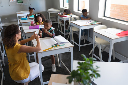 Young caucasian female teacher teaching sign language to african american elementary boy in class....
